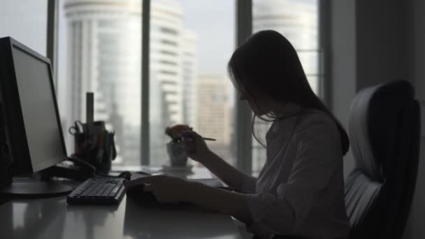 Chica atractiva que trabaja en la oficina. silueta de una mujer de negocios en el fondo de una gran ventana — Vídeo de stock