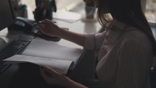 Привлекательная девушка работает с документами после рабочего дня. молодая женщина в деловом костюме сидит за столом в офисе — стоковое видео