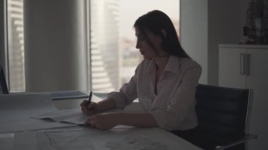 Akşam geç ofiste çalışan bir iş kadın silüeti. Kız masada otururken belgeleriyle çalışır