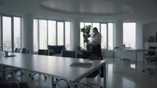 Mulher de negócios anda ao redor do escritório com uma pasta e senta-se à mesa — Vídeo de Stock