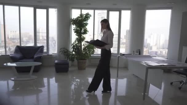 Business woman walking through an empty office with a folder for papers. woman working alone in the evening — Stock Video