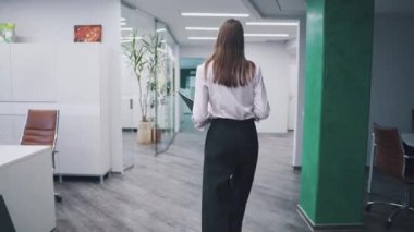 ofis kağıtları onun elinde bir klasörle etrafında çalışan gider. ıssız bir ofiste iş giysili genç kadın. Arkadan Görünüm