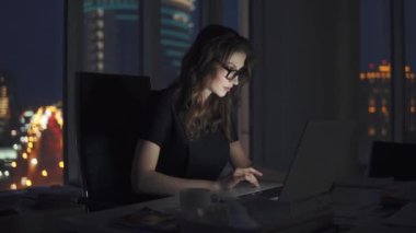 çalışan ofiste geç akşam çalışıyor. kız gece şehrin ışıkları arka plan üzerinde bir dizüstü bilgisayar ile