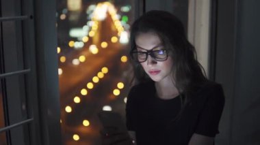 Kız onu bir cep telefonu ile şehrin ışıkları arka plan üzerinde geceleri eller.