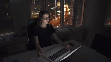 Yöneticisi ofiste geç kadar çalışır. gece şehrin ışıkları karşı gece geç saatlerde bir dizüstü bilgisayarda çalışan genç kadın girişimci.