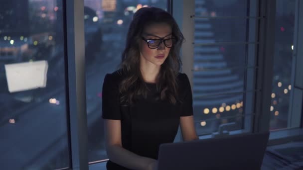 ビジネスの男性は、夜遅くまでオフィスでラップトップに取り組んで。ビジネスの女性は、オフィスの窓辺に座っています。メガネとモニターの反射 — ストック動画