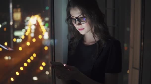 Mulher de negócios jovem à luz de uma tela de telefone celular. menina com um smartphone no fundo bokeh da cidade da noite . — Vídeo de Stock