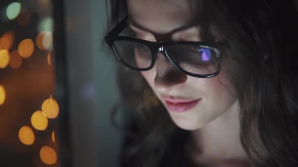 Отражение экрана в очках. Девушка использует смартфон в темноте. портрет молодой женщины на фоне ночного города — стоковое видео