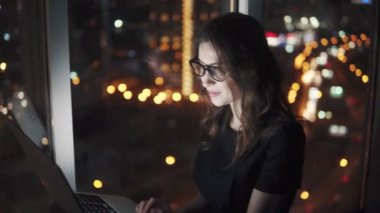 serbest meslek gece şehrin ışıkları arka plan üzerinde bir ofiste bir dizüstü bilgisayar üzerinde çalışıyor. iş kadını geç çalışma kadar oyalandı..