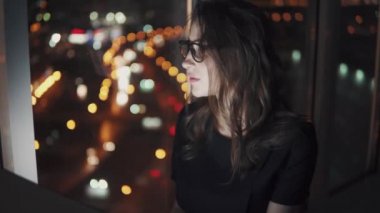 Akşam geç bir dizüstü bilgisayarda çalışan bir çekici kız closeup portresi. Gözlüklü monitör yansımasıdır. gece şehrin ışıkları arasında bir bilgisayarda çalışan genç kadın.
