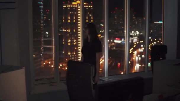 The head goes to an empty dark office after the work day. Portrait of a business woman against the background of the lights of the night city outside the window. — Stock Video