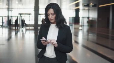 Genç iş kadını modern ofis binası lobide duran bir akıllı telefon kullanır.