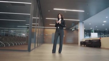 Kendine güvenen iş kadını yakınındaki bir ofis binası konferans odasında dururken bir cep telefonu kullanıyor.