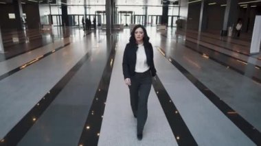 iş takım elbiseli bir kadın modern ofis binası lobi yürür. iş kadını bir cep telefonu kullanır.