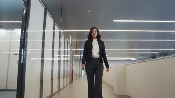 Επιχειρηματικές γυναίκα που περπατά κάτω από την αίθουσα σε ένα κτίριο γραφείων. νεαρή γυναίκα σε ένα μαύρο επαγγελματικό κοστούμι. — Αρχείο Βίντεο
