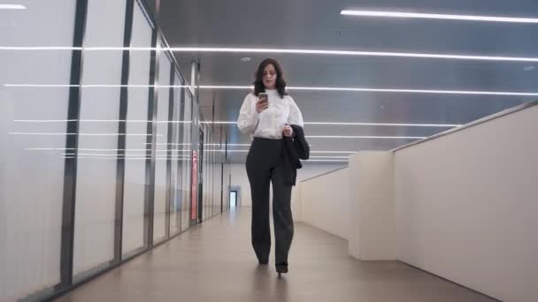 自信を持ってビジネスの女性は、携帯電話を使用します。事務所ビルを歩いてビジネス スーツの女の子. — ストック動画