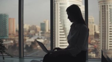 Genç kadın rahat büyük bir pencere yakın oturan bir laptop üzerinde çalışıyor.