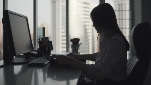 Silhouet van een jong meisje werken met documenten in het kantoor. zakelijke vrouw zittend aan de computer bureau. — Stockvideo