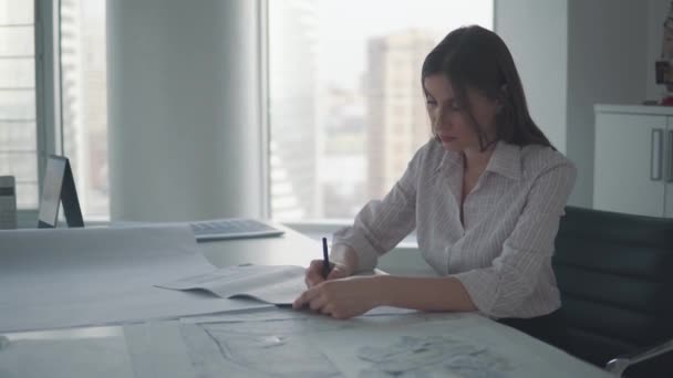 Jonge zakelijke vrouw werken met documenten en tekeningen zittend aan de tafel in het kantoor. — Stockvideo