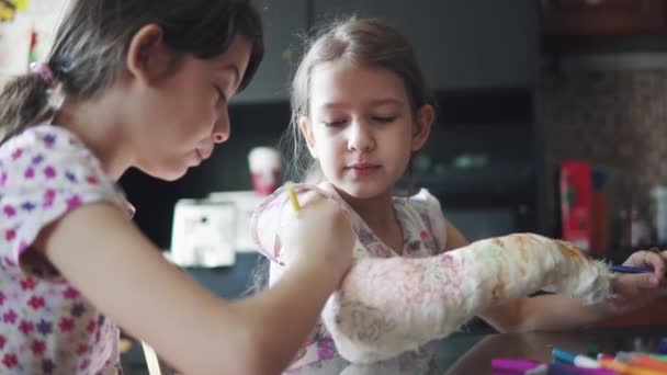 Kinderen schilderen een gebroken arm in een verband. zus probeert op te vrolijken en hangen een zieke zus. — Stockvideo