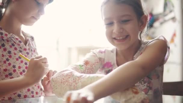Criança se baseia em gesso. a menina pinta uma mão rebocada para sua irmã. namorada se preocupa com um amigo doente . — Vídeo de Stock
