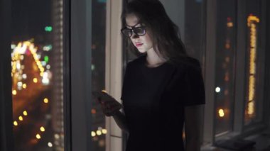 smartphone ekran ışığında genç bir kızın portresi. Kız bir cep telefonu gece şehrin arka planı kullanır