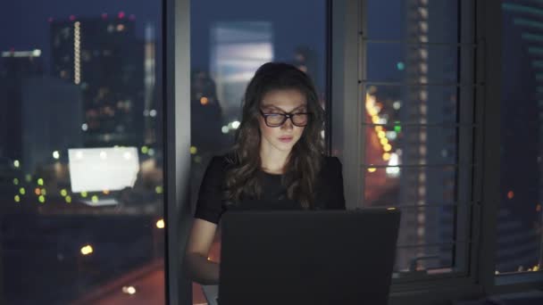 Jeune femme d'affaires travaillant tard dans le bureau. portrait d'une fille avec des lunettes sur le fond de la ville nocturne — Video