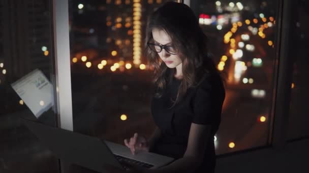 Detailní portrét atraktivní dívka, pracovat na notebooku v pozdních večerních hodinách. odraz na monitoru s brýlemi. mladá žena pracuje na počítači uprostřed světla noční město. — Stock video