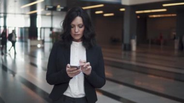 iş takım elbiseli bir kadın modern ofis binası lobi yürür. iş kadını bir cep telefonu kullanır.
