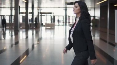 iş takım elbiseli genç bir kadın bir modern ofis binasının lobisinde yürür.