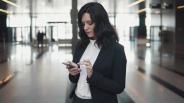 Modern bir ofis binasının lobisinde ayakta iken bir cep telefonu üzerinde manifatura genç kadın.