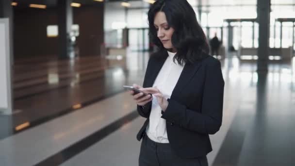 Retrato de una mujer de negocios con un teléfono en sus manos. mujer joven en el vestíbulo de un edificio de oficinas — Vídeos de Stock