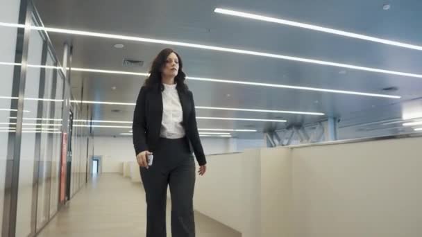 Vertrouwen zakenvrouw lopend onderaan de zaal in een kantoorgebouw. jonge vrouw in een zwart pak. — Stockvideo