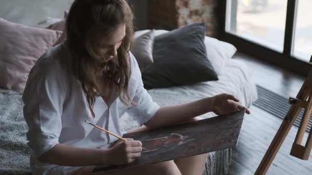 La fille artiste peint un tableau dans le home studio. L'artiste travaille sur une peinture le matin . — Video