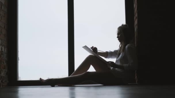Silhouette of a girl artist writing a picture near a large window. — Stock Video