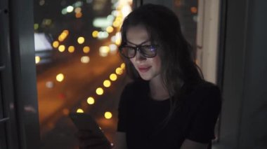 Kız onu bir cep telefonu ile şehrin ışıkları arka plan üzerinde geceleri eller.