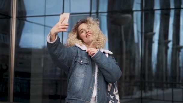 Mooie krullend meisje maakt selfie. Portret van een meisje met een charmante glimlach die zich op de camera van de smartphone schiet. — Stockvideo