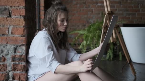 Artiste peint un tableau dans un home studio dans le style d'un loft. portrait d'une jolie fille travaillant dans une atmosphère détendue . — Video