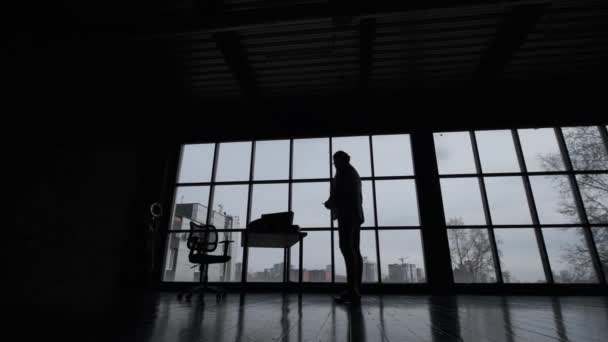 Silhouette eines Mannes in einem geräumigen Büro vor dem Hintergrund eines großen Fensters. — Stockvideo