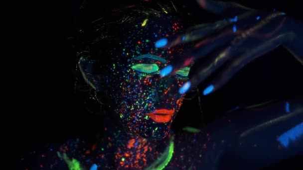 Flickor ansikte i neonljus. Porträtt av en flicka målad med glödande färg. — Stockvideo