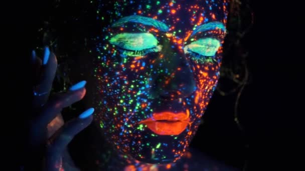 Glow paint on the girls face. Closeup portrait of a beautiful young woman with glowing paint on her face. — Stock Video