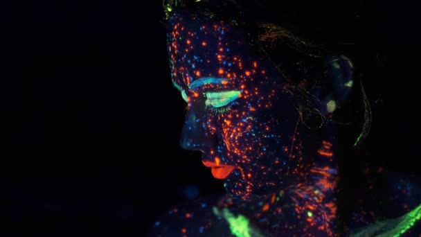 Neon paint on the girls face. portrait of a young woman painted with luminous paints. — Stock Video