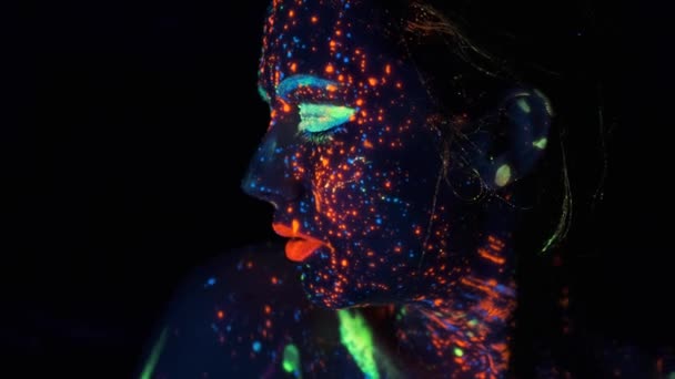 Πορτραίτο μιας νεαρής γυναίκας ζωγραφισμένη με φωτεινές μπογιές. χρώμα νέον στα κορίτσια πρόσωπο. — Αρχείο Βίντεο