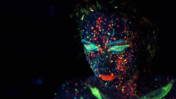 Meisjes gezicht in neon licht. Portret van een jonge vrouw gekleurd met lichtgevende verven. — Stockvideo