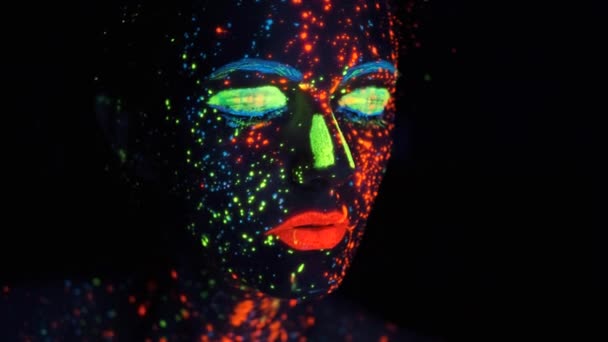 Måla glödande i ultraviolett ljus. Porträtt av en flicka målad med glödande färg. — Stockvideo