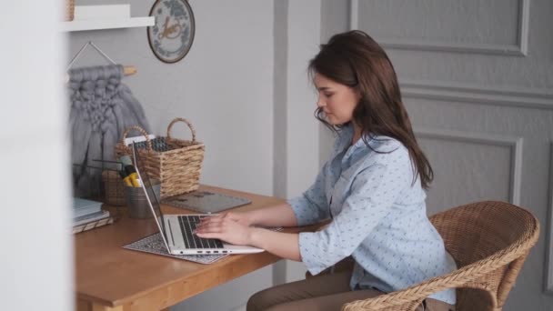 Bir ev stüdyosunda çalışan çekici bir genç kadının portresi. Freelancer bir dizüstü bilgisayar üzerinde çalışıyor. — Stok video