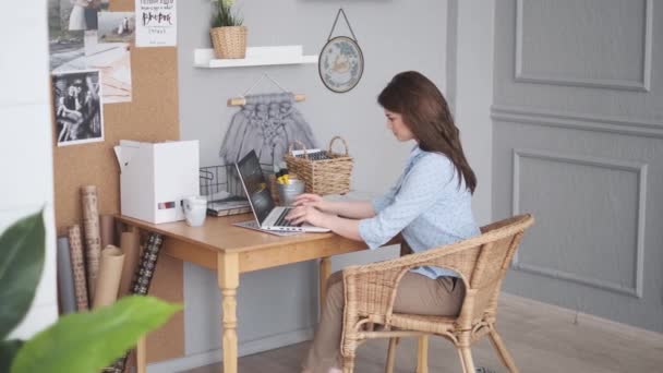Mujer joven que trabaja en casa en un ordenador portátil. chica en un lugar de trabajo cómodo — Vídeo de stock