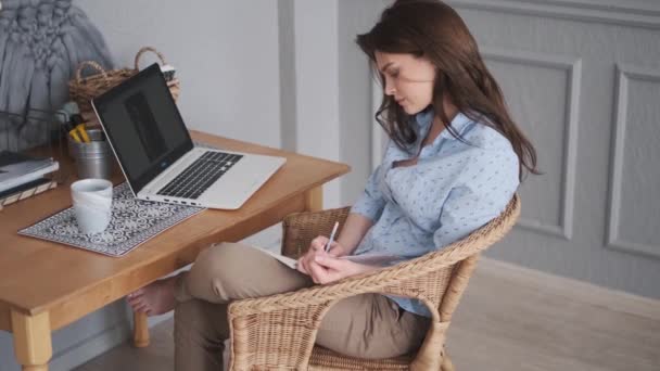 Porträt einer jungen Freiberuflerin in einem gemütlichen Home-Studio. Mädchen macht sich Notizen mit Stift in Notizbuch. — Stockvideo