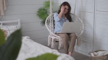 kız rahat bir asılı sandalyede kucağında bir dizüstü bilgisayar ile oturuyor. evde çalışan genç kadın serbest çalışan.