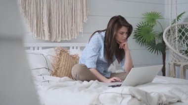 kız yatakta otururken bir dizüstü bilgisayar kullanır. Evde rahat çekici bir genç kadın portresi.